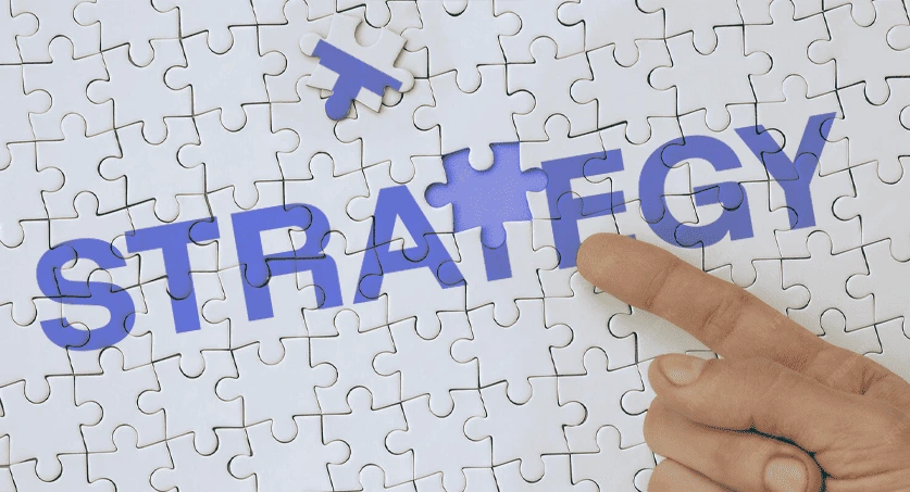 Quebra cabeça com a palavra strategy escrita em azul e fundo branco, representando estratégias de marketing digital