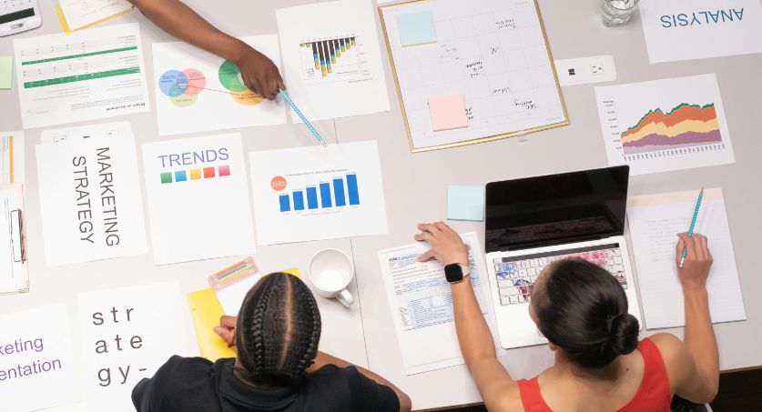 Equipe de três especialistas de uma agência de marketing em uma mesa com vários papéis de plano de ação para estratégias de marketing