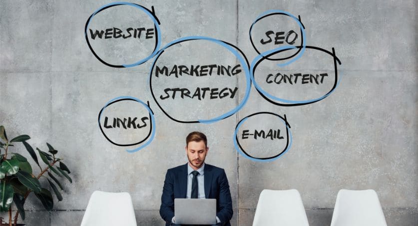 Homem sentado em cadeira escreve em notbook e acima dele está escrito um mapa mental com estratégias de inbound marketing