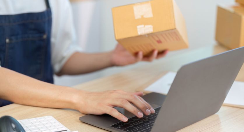 Homem na frente de computador segurando caixas de estoque sazonal