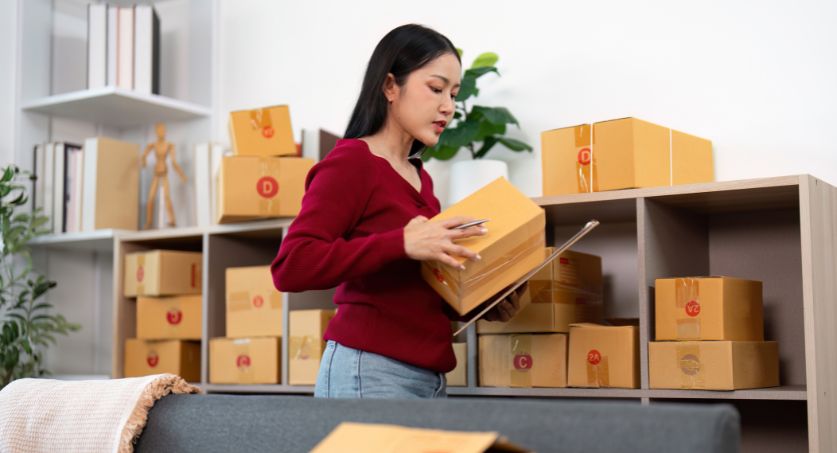 Mulher em pé em frente a prateleira cheia de caixas organizando estoque sazonal