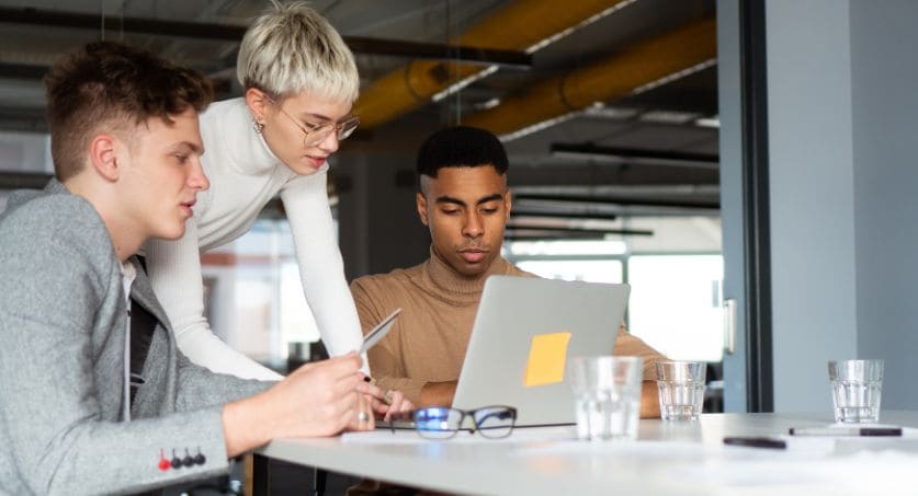 Equipe de marketing de 2 homens e uma mulher em um escritório na frente de um computador analisando estratégia omnichannel