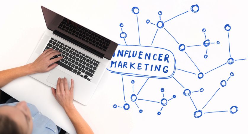 Pessoa usando notebook ao lado de ilustração sobre marketing de influência, com conexões desenhadas em azul sobre fundo claro.
